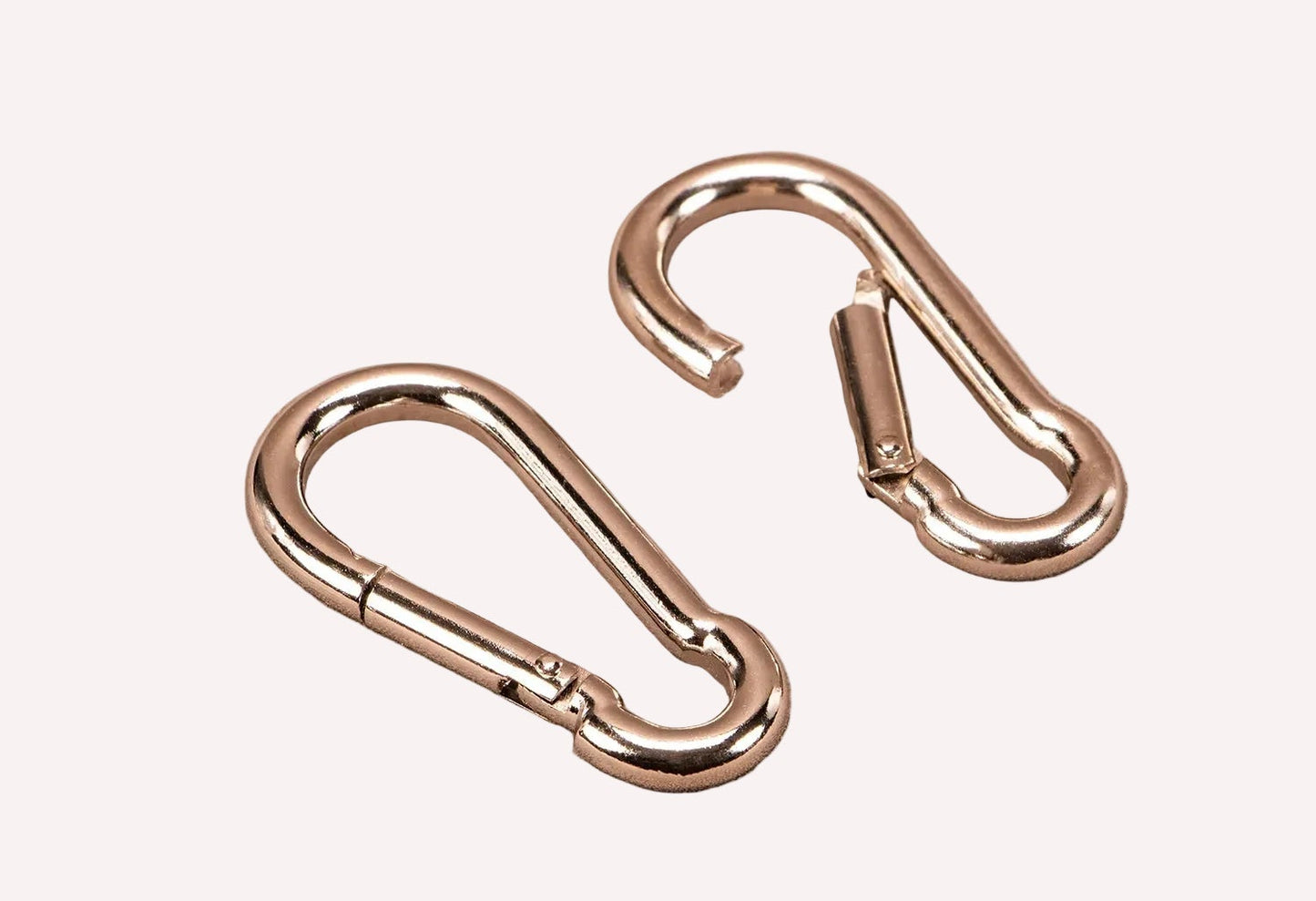 Two metallic carabiners on a beige background